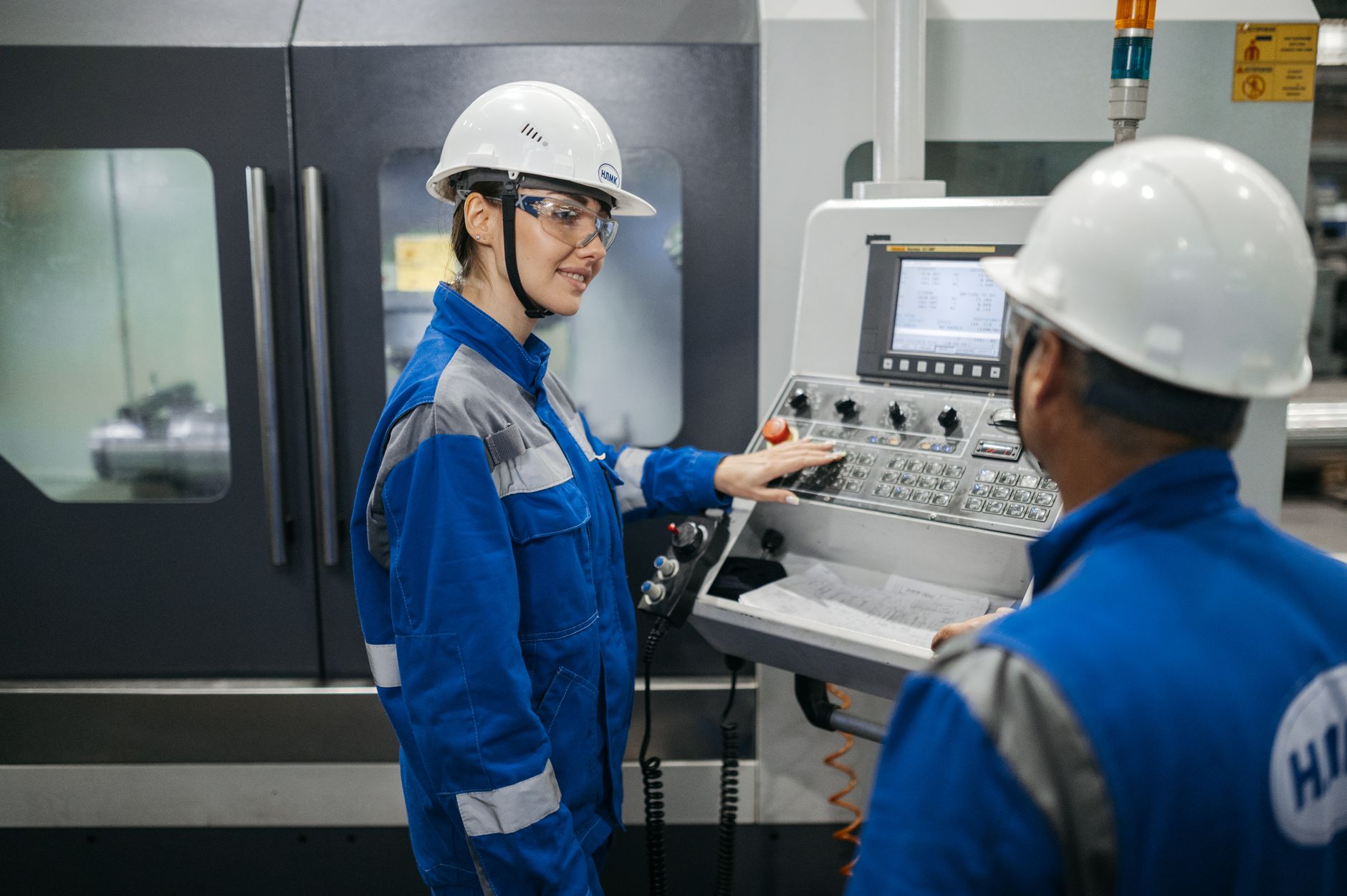 Two engineers in protective gear operating equipment on a factory floor